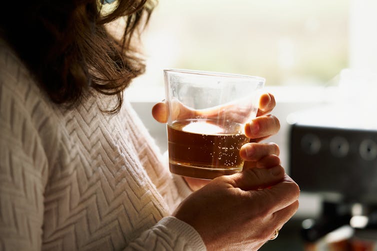 Close-up of a person holding a glass of whiskey in both hands