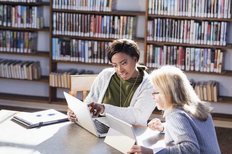 Two women work on laptops at a library.