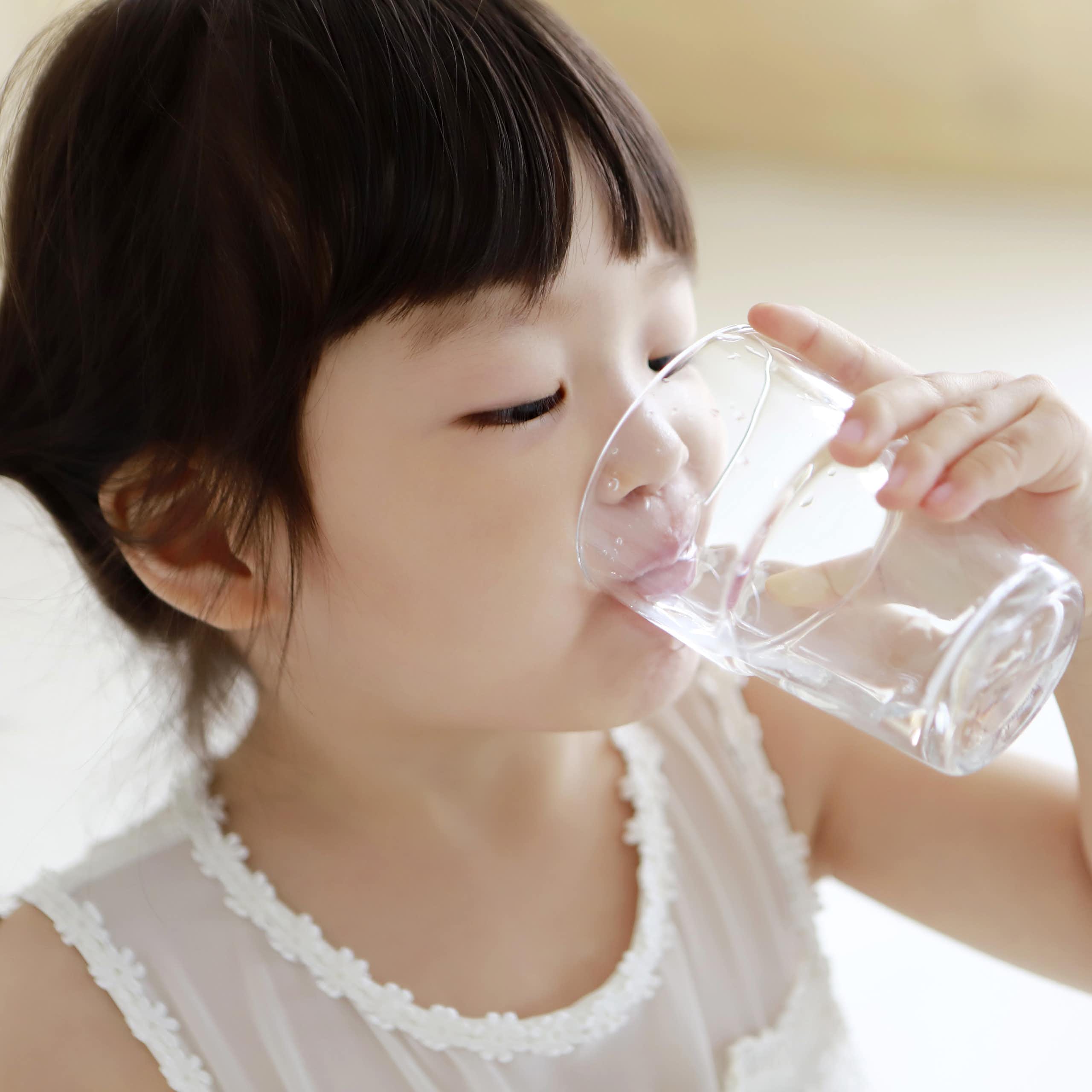A little girl drinks a glass of water.