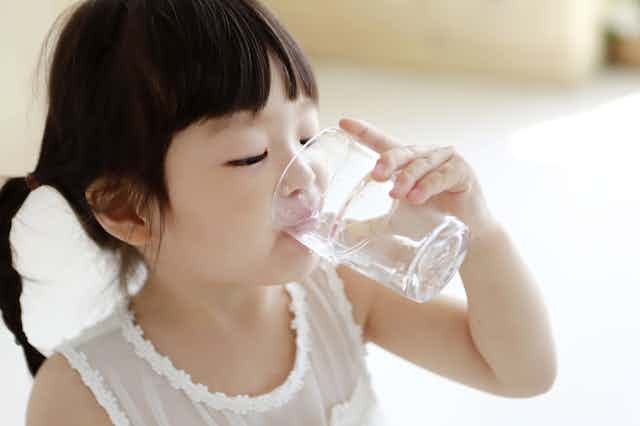 A little girl drinks a glass of water.