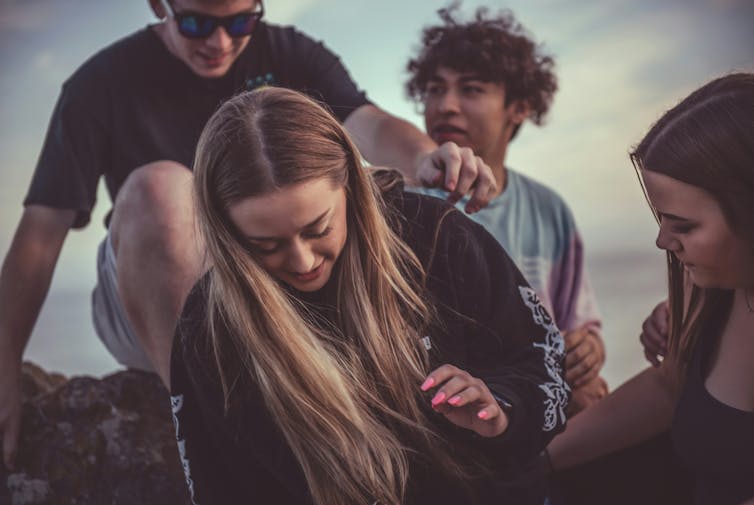 Teens sit on a rock by the ocean