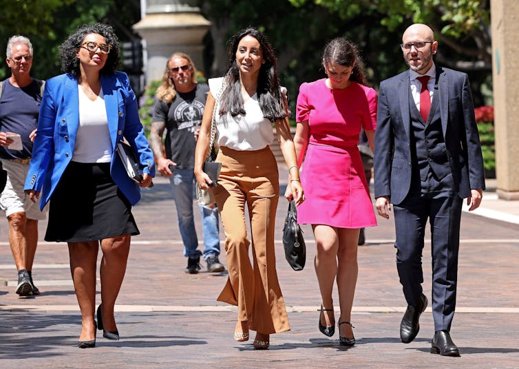 A woman walks down a street with another woman on her left and a man and woman on her right