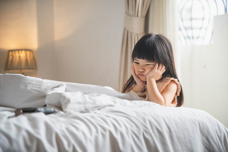 Child sits next to her parent's bed