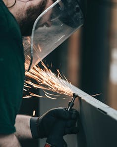 Man wearing a plastic mask cuts material with an angle grinder, sparks fly