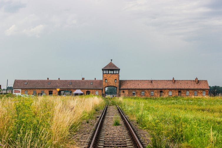 a low red building in the distance with train tracks leading to its centre