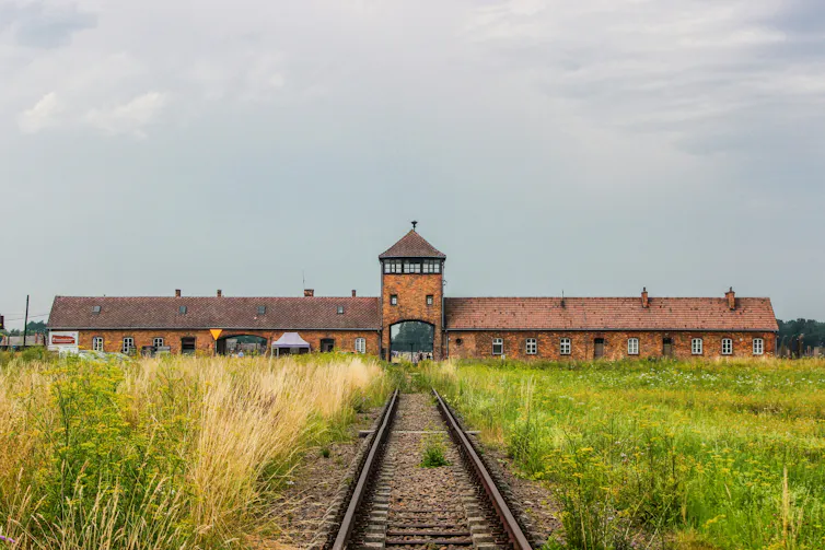 a low red building in the distance with train tracks leading to its centre