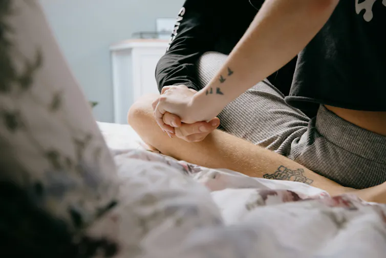 A young couple partially out of frame holding hanfs while sitting on a bed.