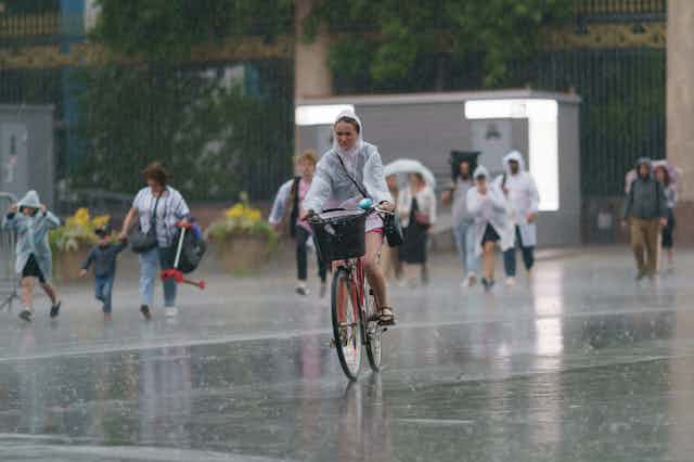 A woman cycles in the rain with people walking behind her