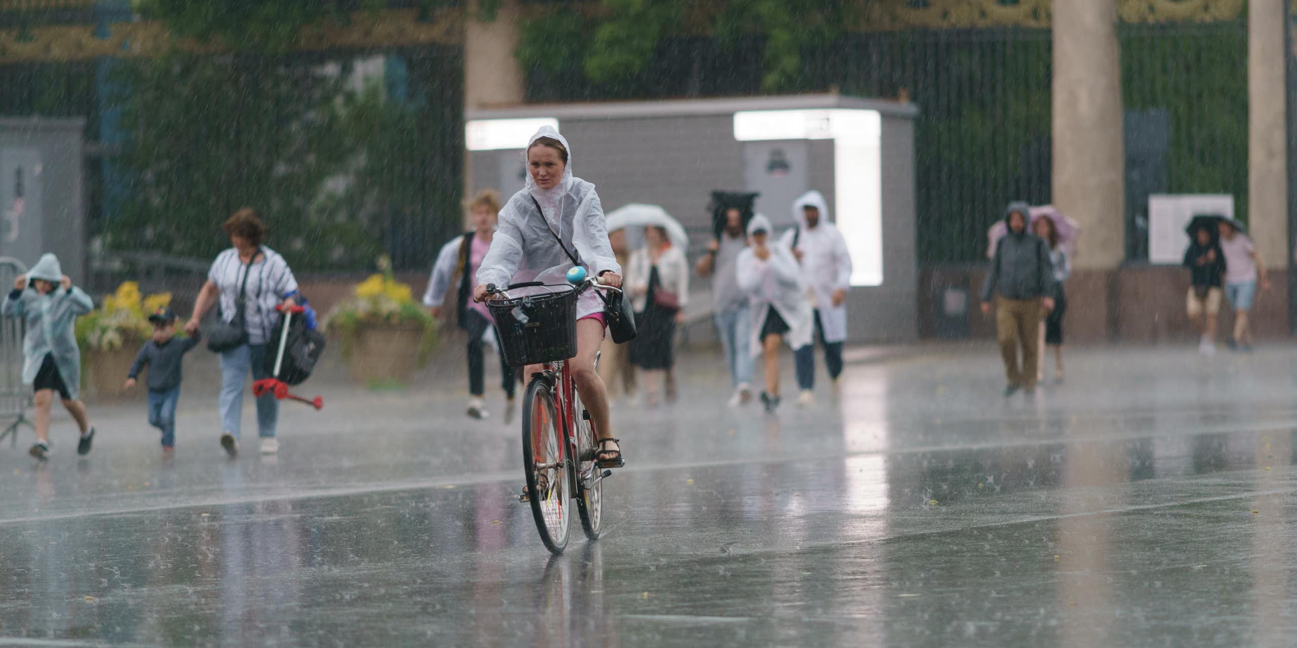 A woman cycles in the rain with people walking behind her