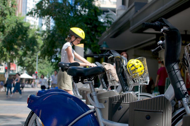 A woman wearing a helmet prepares to take a ride-share bike from a stand