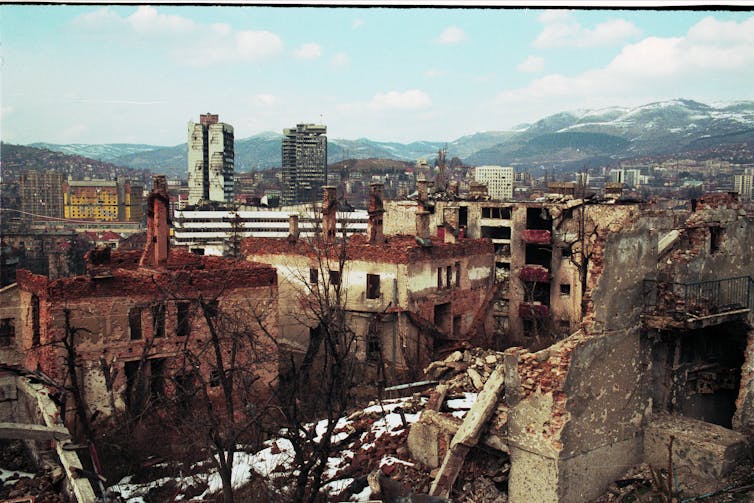 A panorama of a war-damaged city against a backdrop of snow-capped mountains.