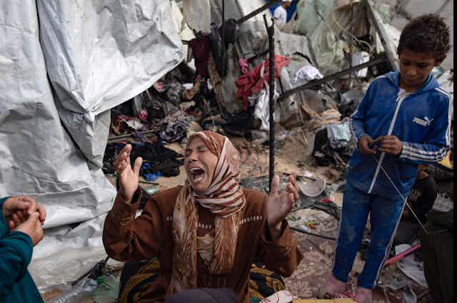 A woman on her knees crying as she inspects damage to her her tent.