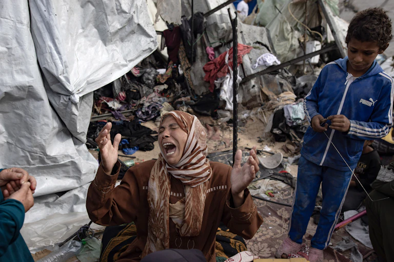 A woman on her knees crying as she inspects damage to her her tent.