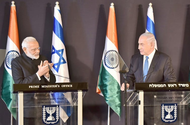 Narendra Modi and Benjamin Netanyahu face each other on a stage in front of Indian and Israeli flags.