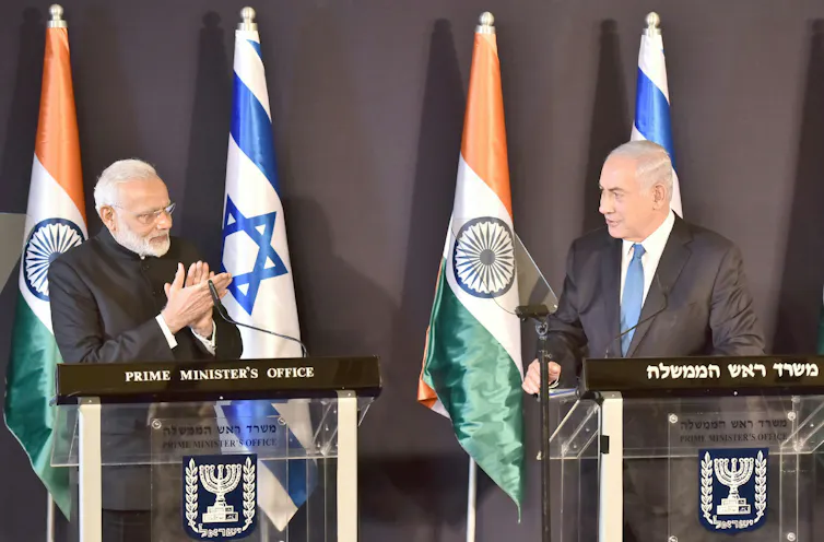 Narendra Modi and Benjamin Netanyahu facing each other on a stage in front of Indian and Israeli flags.