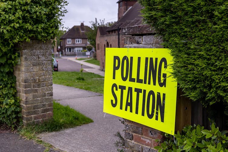 A yellow polling station poster on a gate post.