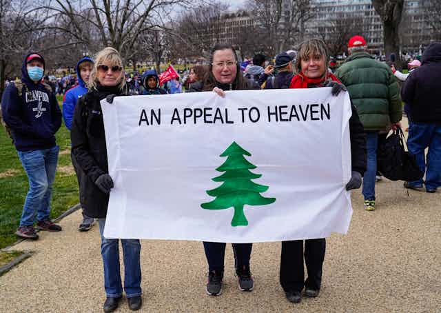 People stand holding the 'Appeal to Heaven' flag.