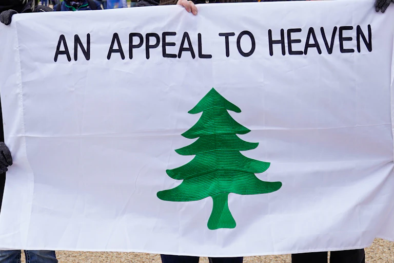 People stand holding the 'Appeal to Heaven' flag.