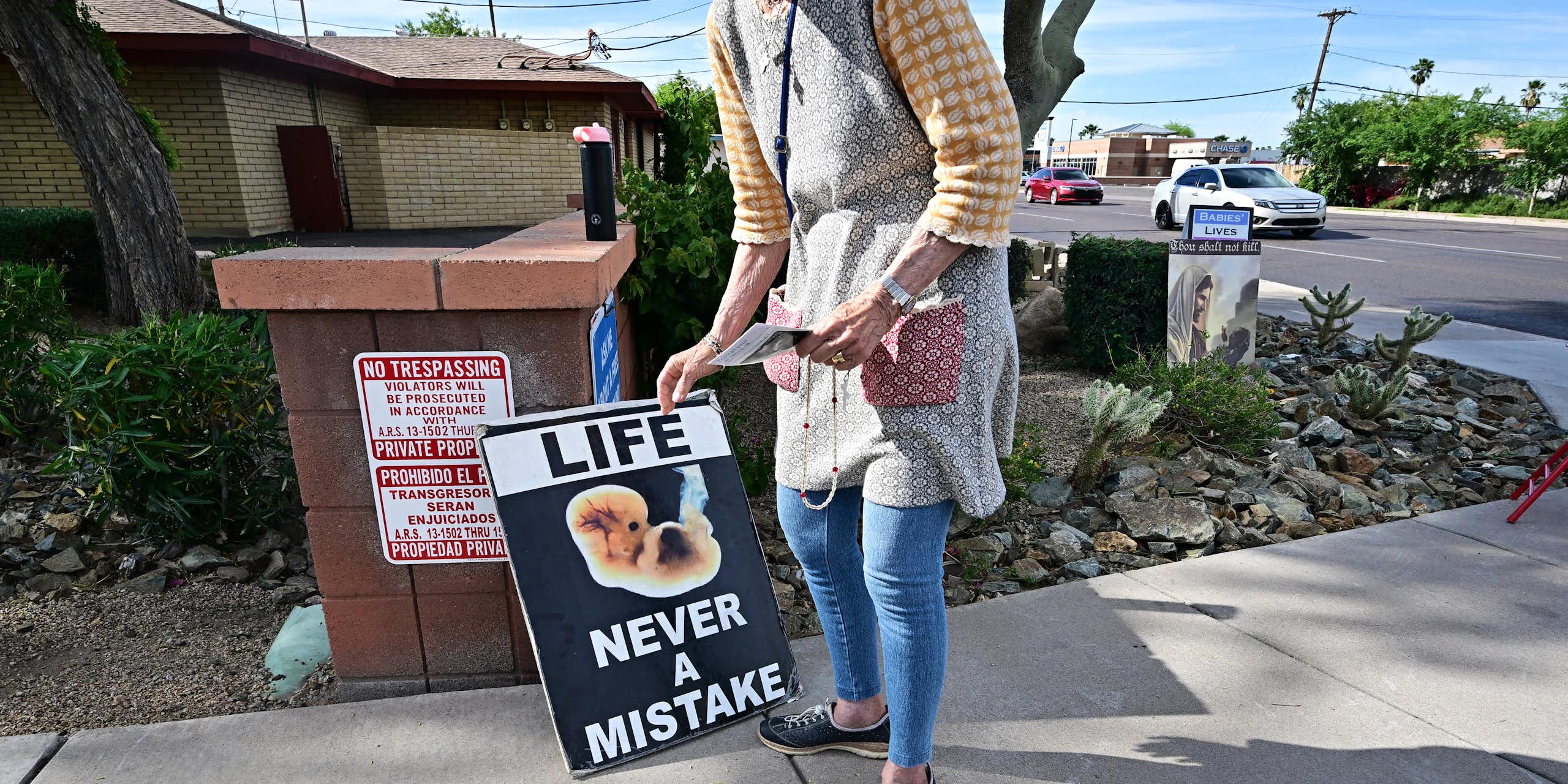 A woman is seen from the neck down holding a sign that says 'Life never a mistake,' with a photo of a very small fetus. 