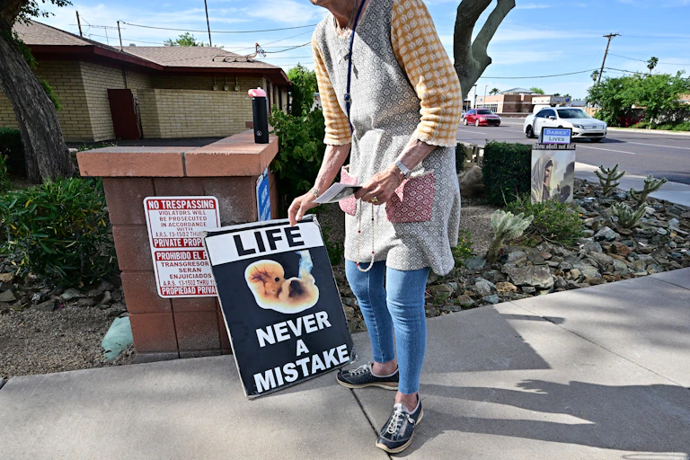 A woman is seen from the neck down holding a sign that says 'Life never a mistake,' with a photo of a very small fetus.