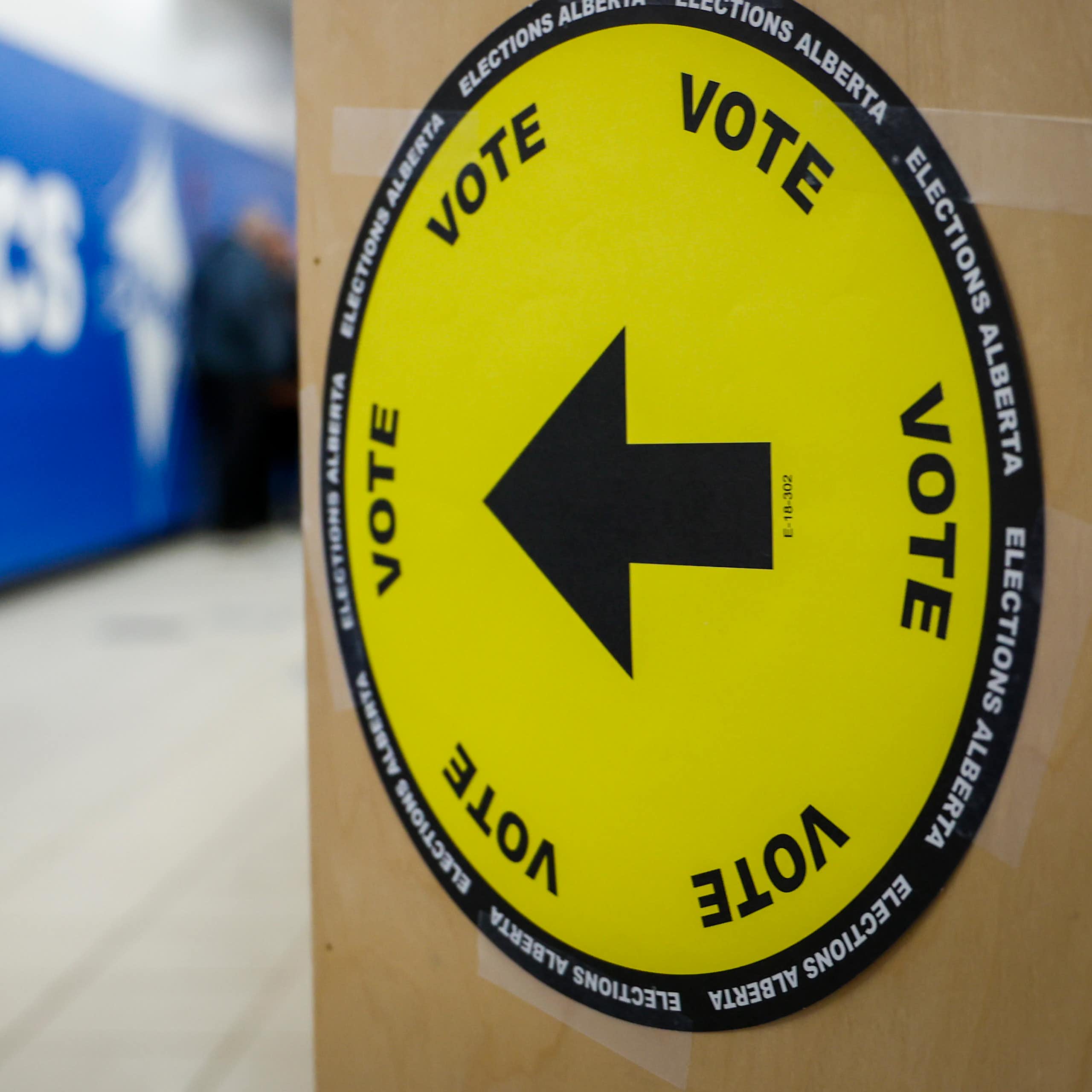A man walks past a yellow vote sign with an arrow.