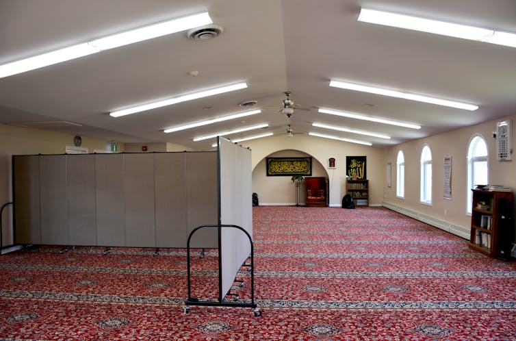 A prayer hall in a mosque. A grey divider separates a section reserved for women from the rest of the space.