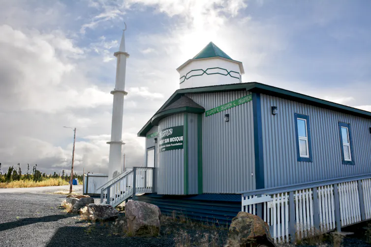 A grey building with a white minaret and green dome.
