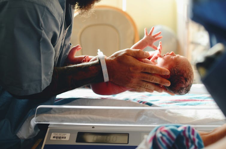 Close-up of a person holding a premature baby over a scale