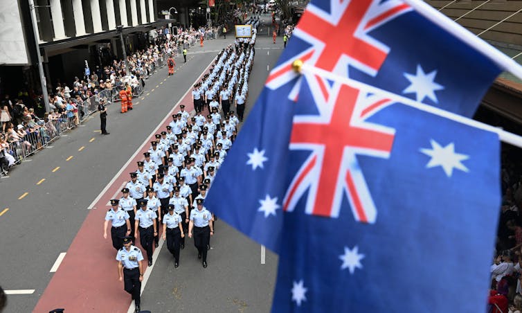 Two out of focus Australian flags in front of rows of Air Force personnel marching in a parade
