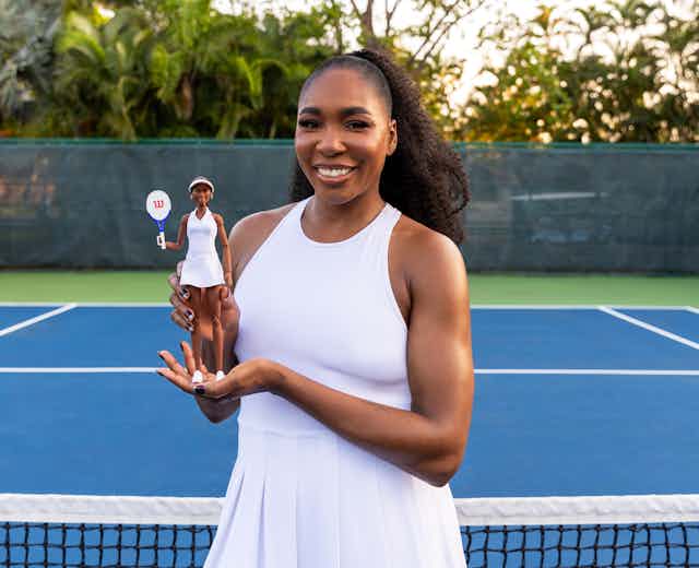Venus Williams holds a Barbie with her likeness on a tennis court. 