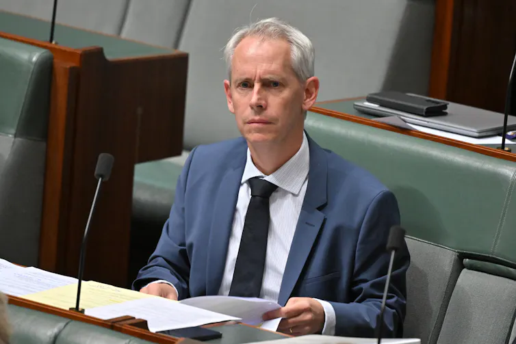 A man in a suit frowns as he holds documents