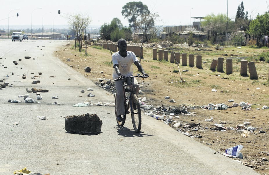 A person cycles on a road strewn with rubble and trash.