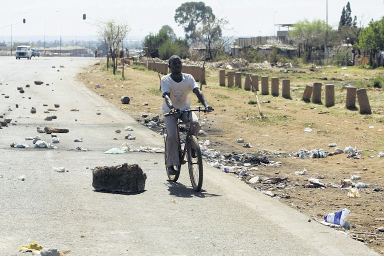 A person cycles on a road strewn with rubble and trash.
