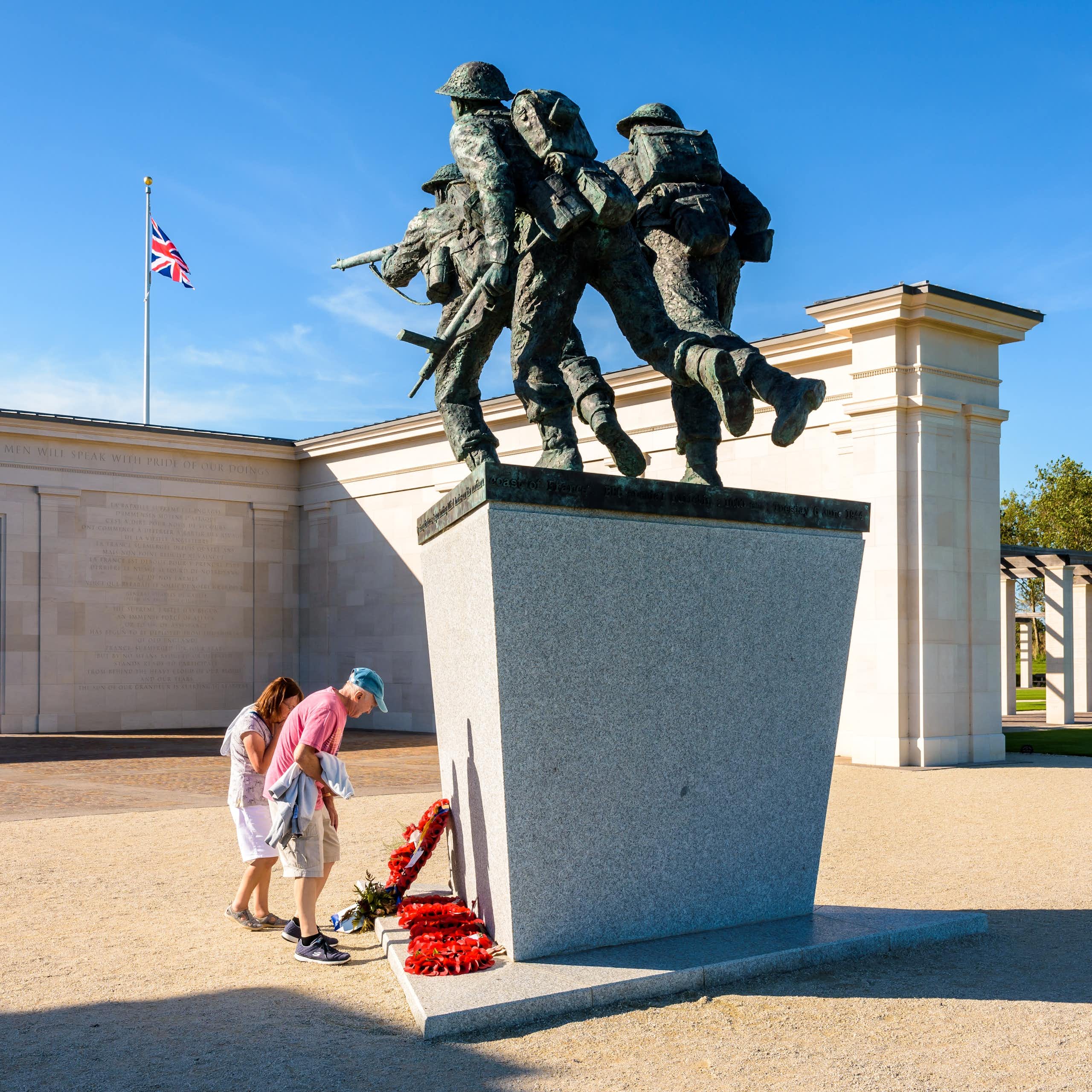 Deux personnes se recueillent au pied d'un monument commémoratif. Derrière, on voit le drapeau britannique.