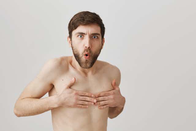 Man naked from waist up, making a face and holding his hands over his nipples