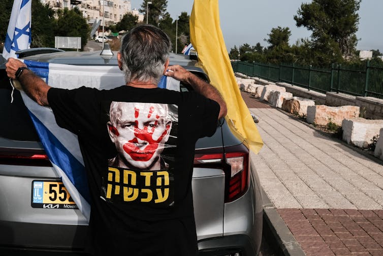 A man wearing a t-shirt with a picture of Benjamin Netanyahu with a bloody face, part opf an anti-government protest.