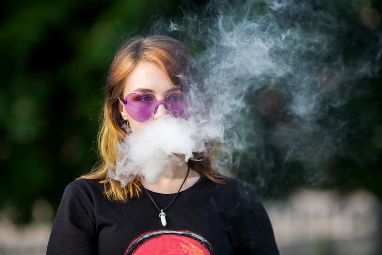 Une jeune fille souffle de la vapeur de cigarette électronique.