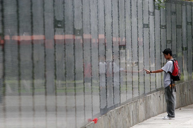 A boy touches a large stone wall with thousands of names etched on it.