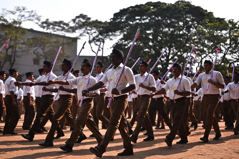 A group of Indian men wearing white shirts and holding flags marching in unison.