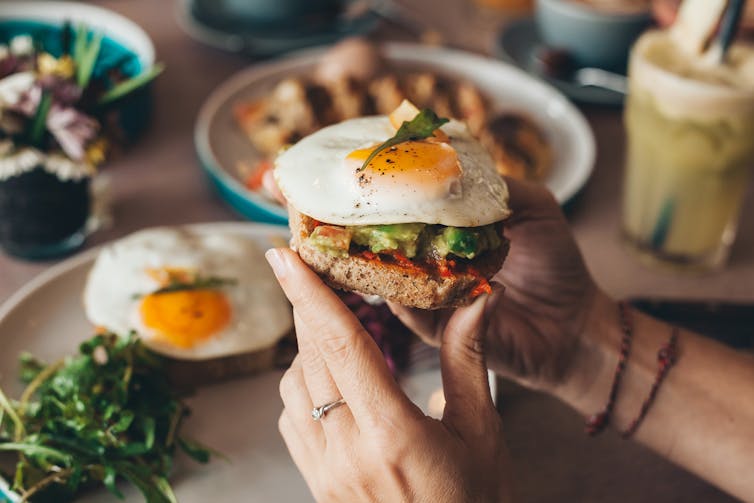 Una persona sosteniendo una tostada con huevos y aguacate.