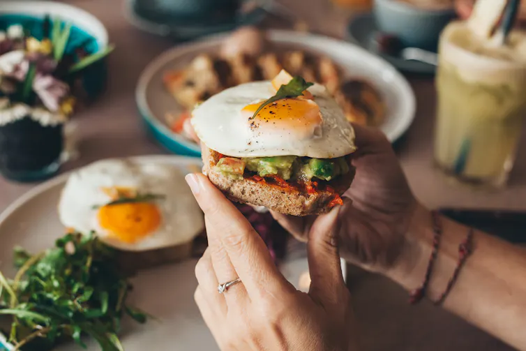 A person holding a piece of toast with eggs and avocado.