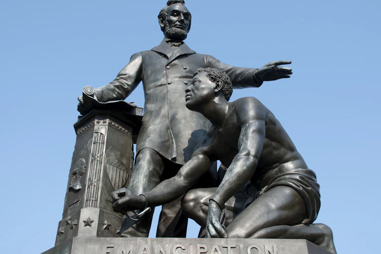 A man towering over another who is kneeling on a pedestal which has the word 'Emancipation' engraved on it.