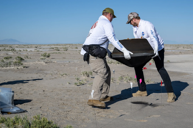 Two people carrying the sample return capsule, which is a black box. 