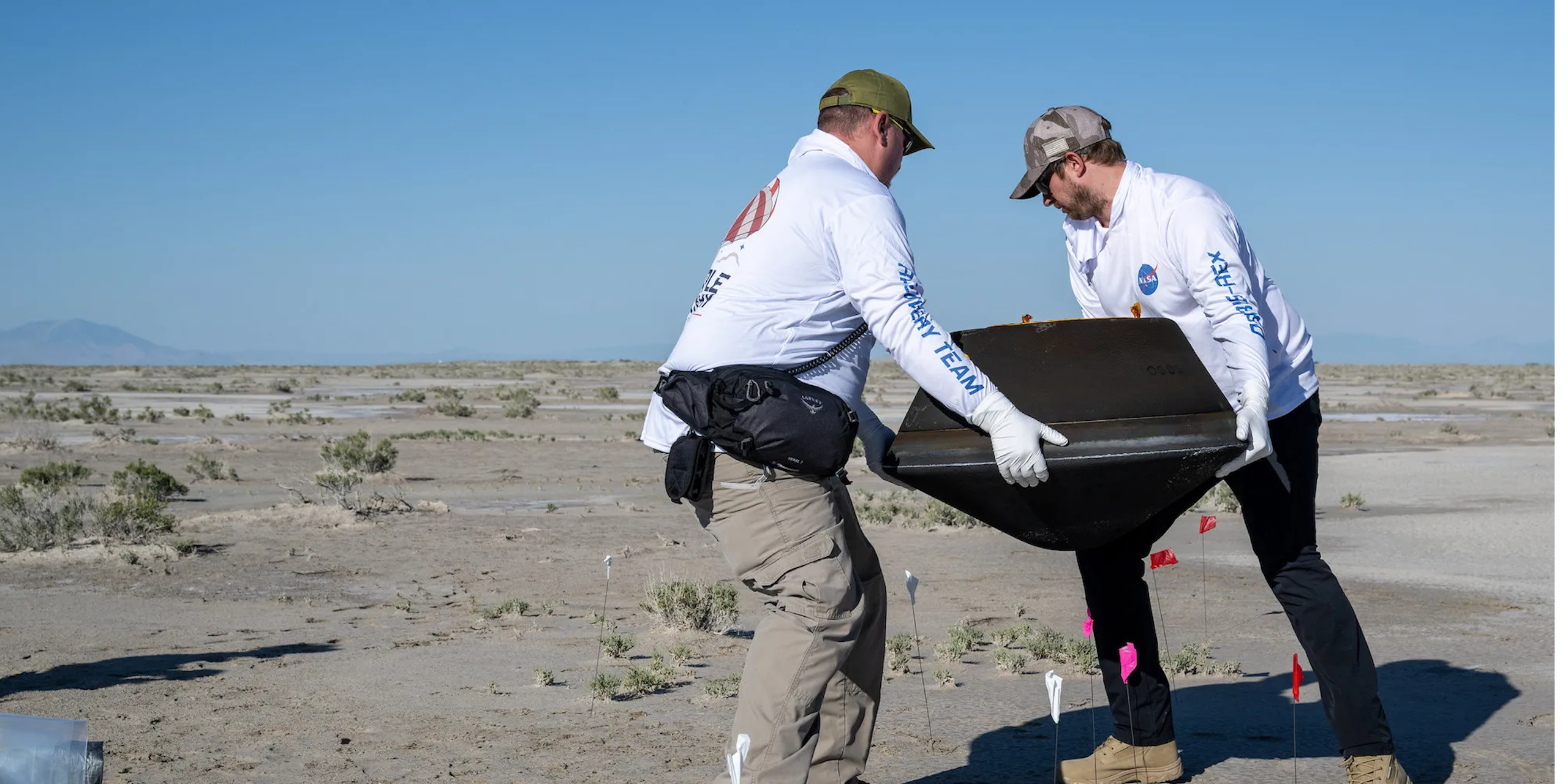 Two people carrying the sample return capsule, which is a black box. 