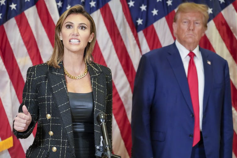 A man and a woman standing in front of several American flags.