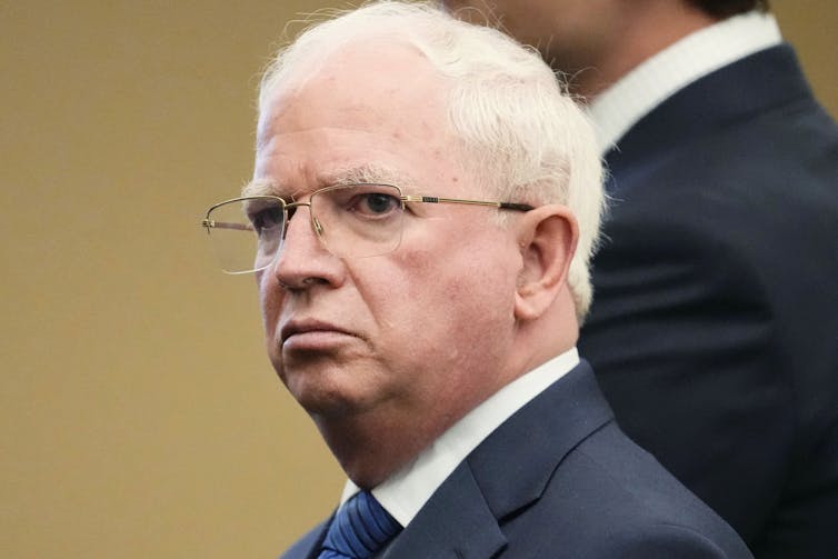 A white haired man with glasses in a suit and tie.