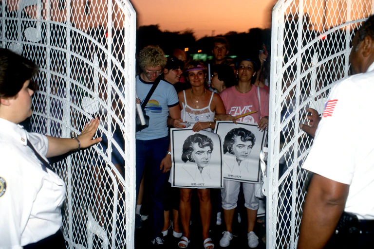 Two police officers stand behind a white, wrought iron gate as fans crowd together on the other side.