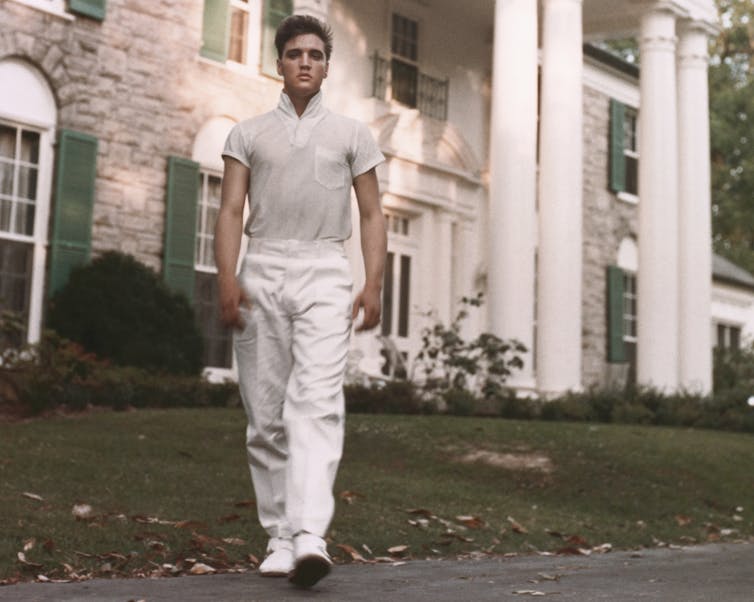 Young man walks towards camera with a mansion in the background.