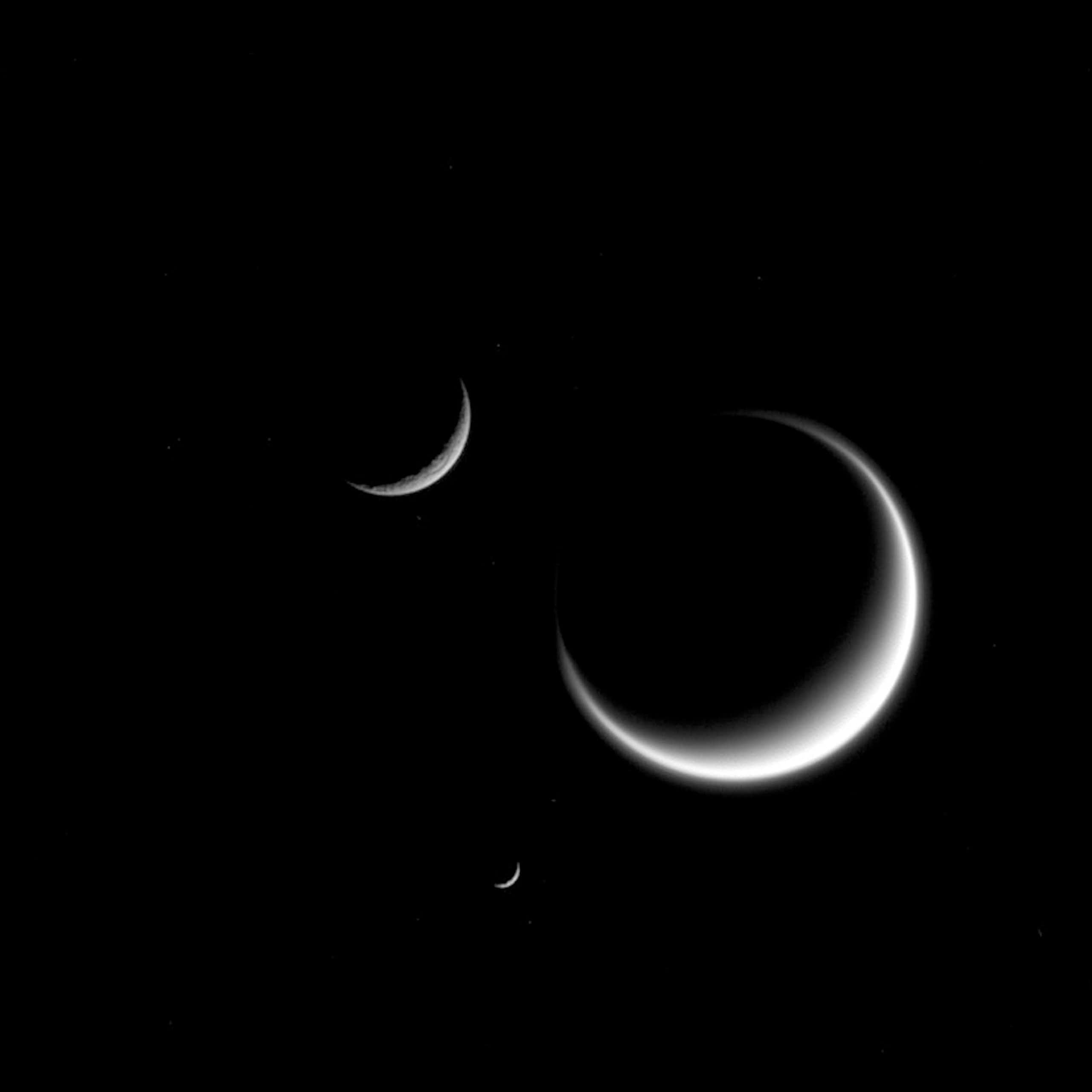 Three moons, shown partially shadowed, in space. 