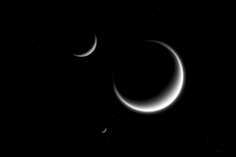 Three moons, shown partially shadowed, in space.